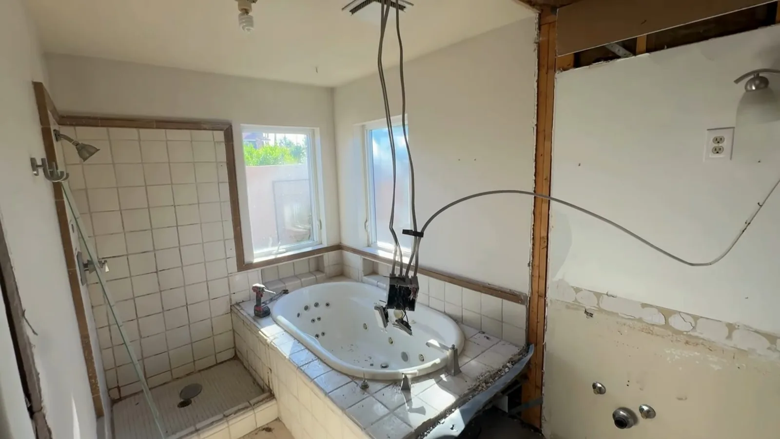 Bathroom with a wall section cut open beside a tiled tub surround and wires hanging from the ceiling
