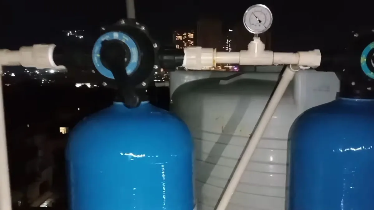 Two blue pressure tanks joined by white pipe with a round gauge, photographed at night