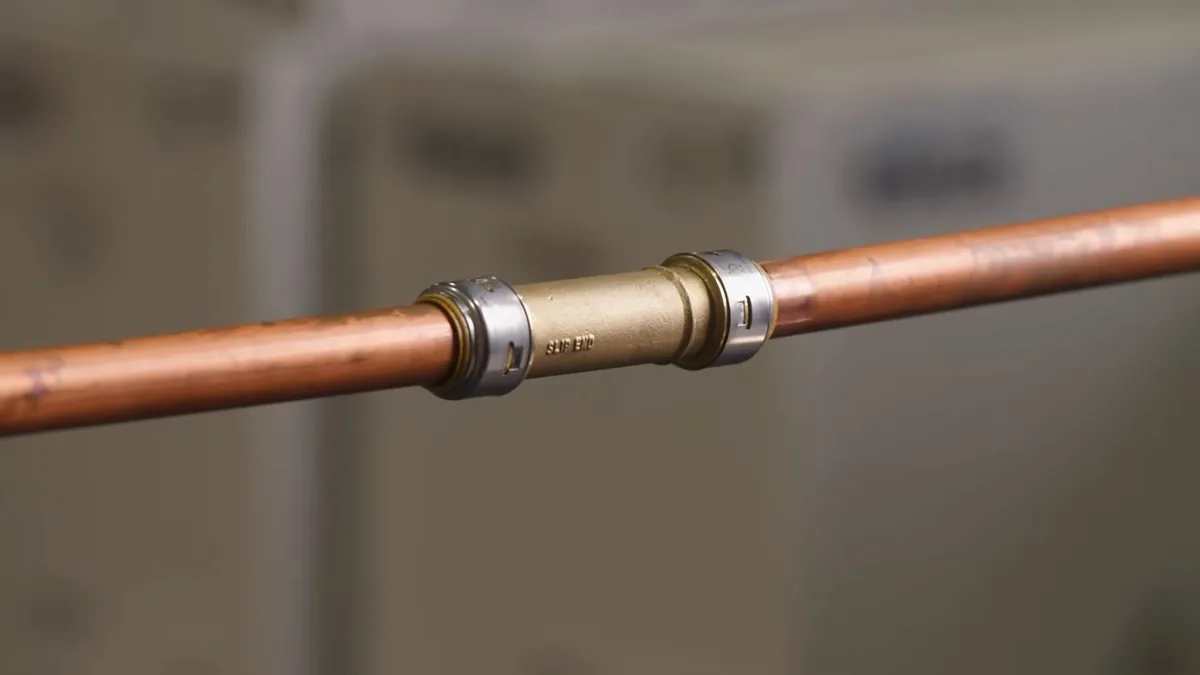 Copper pipe joined by a brass push-fit coupling against a soft grey background