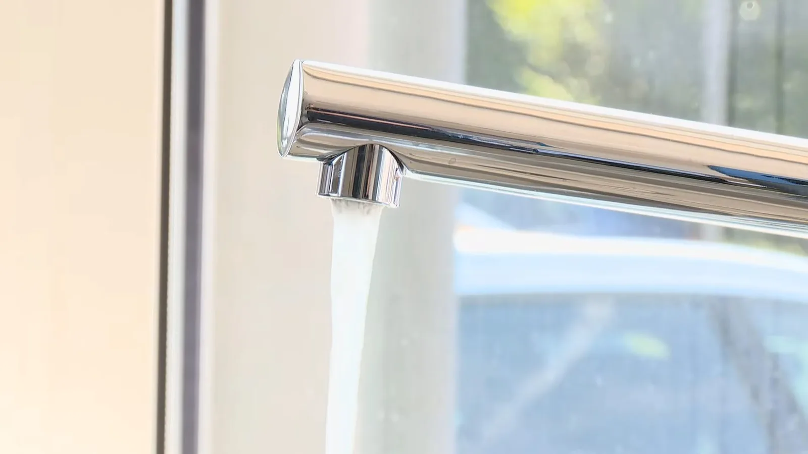 Chrome kitchen faucet running a clear stream of water beside a window