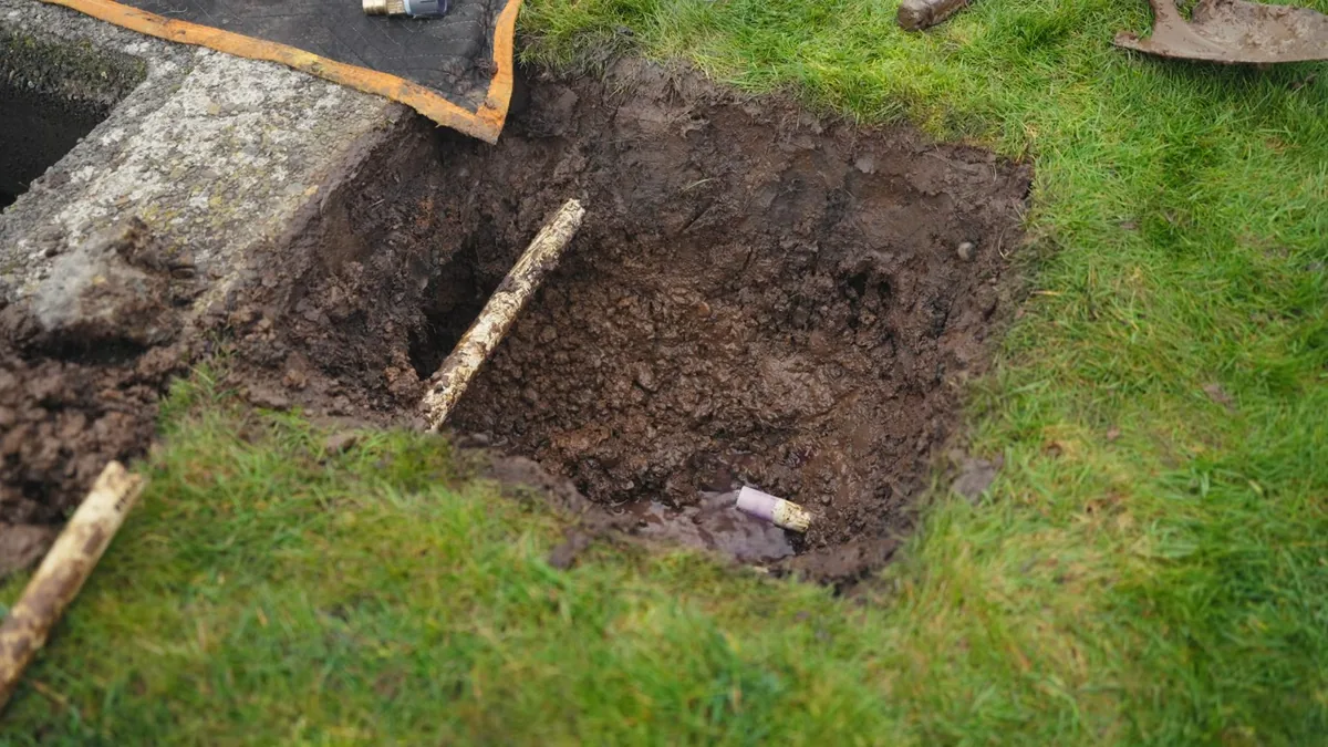 Square hole dug in a lawn with a service pipe visible at the bottom