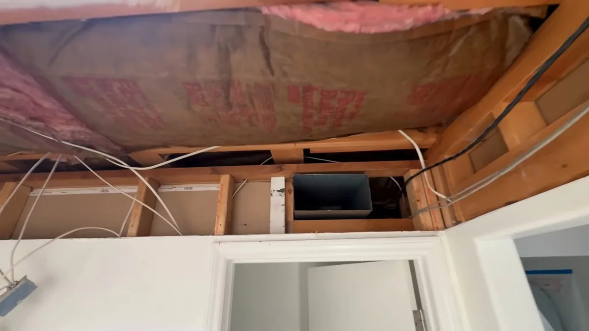 Exposed ceiling framing with pink insulation, wiring and a duct opening above a white door frame