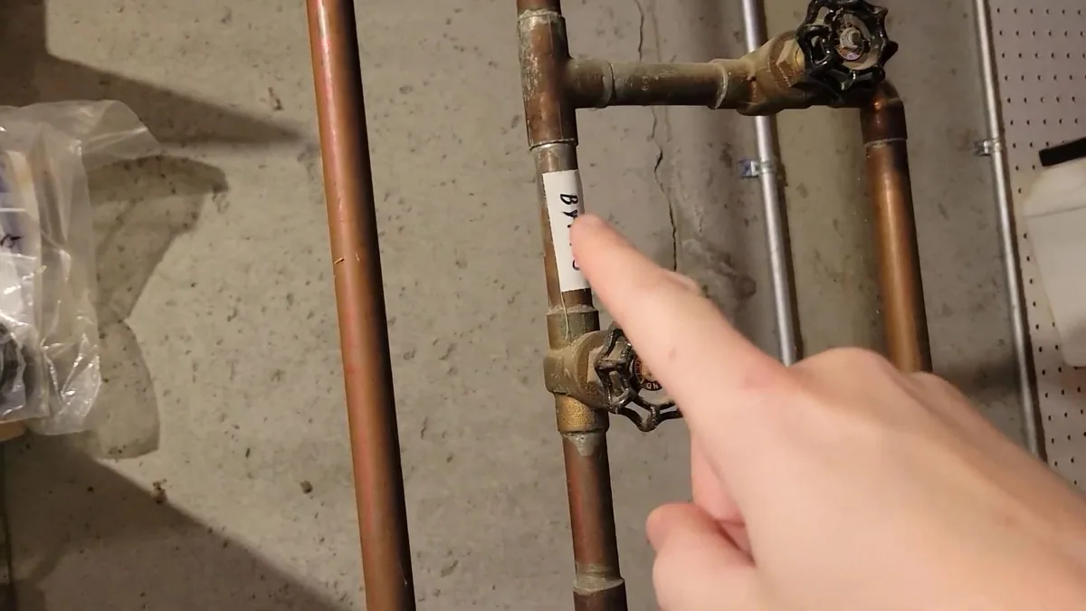 Finger pointing at a paper tag on a copper pipe between two brass shutoff valves
