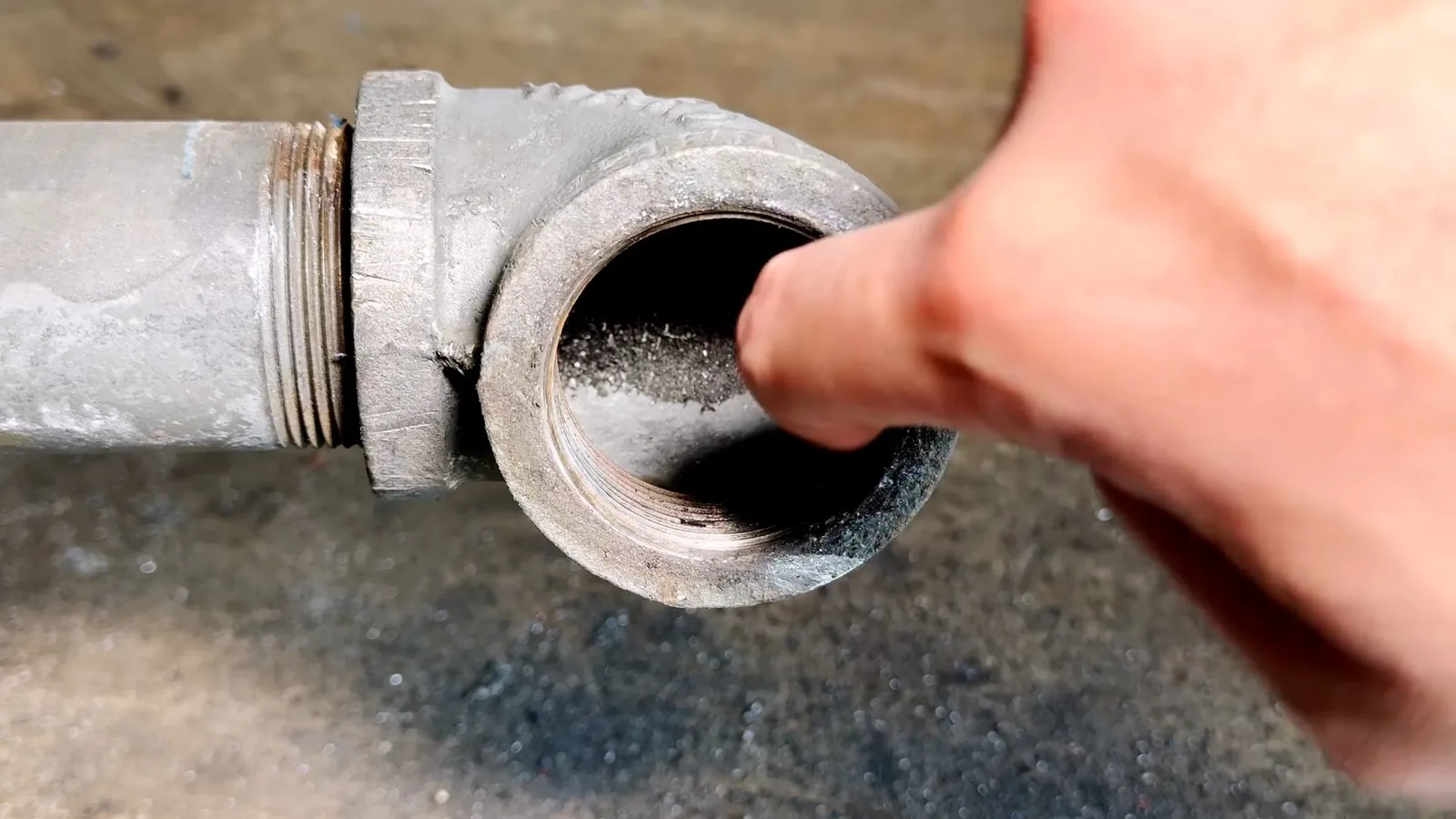 Finger touching debris inside the open threaded end of a galvanized cleanout fitting