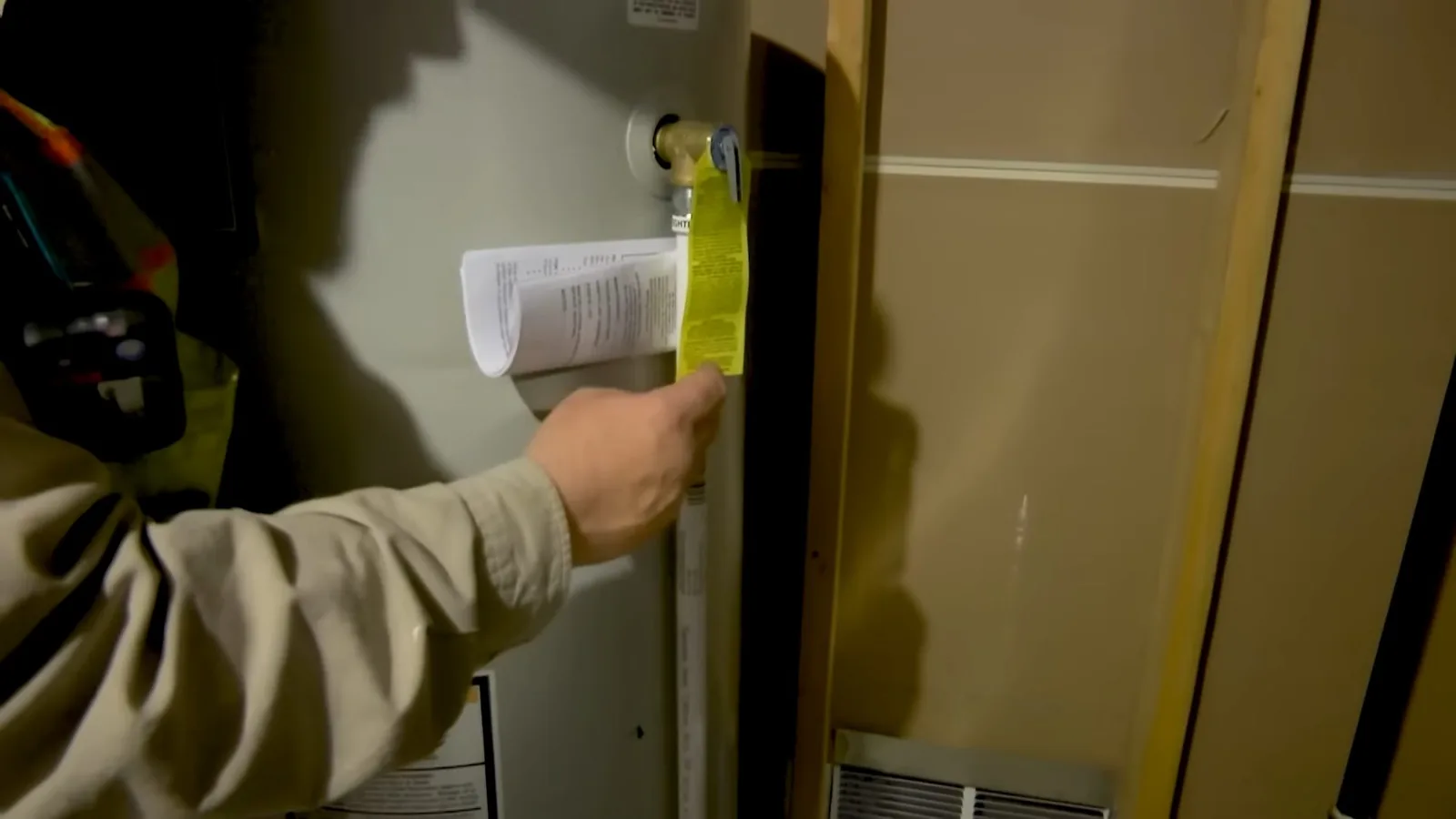 Hand holding a printed sheet against the yellow label on a water heater inside an open closet