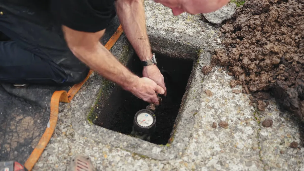 Man's hand reaching into a concrete meter box to read a water meter set in the ground