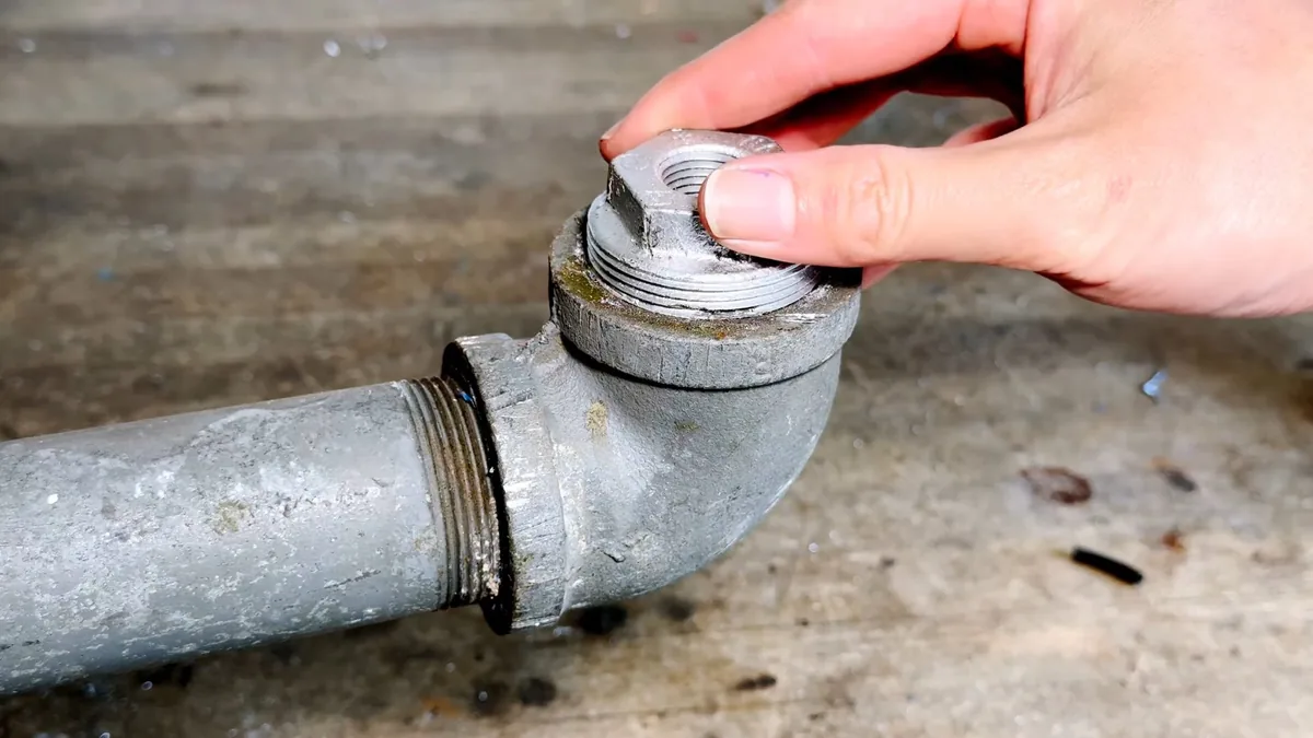 Hand unscrewing the threaded cap from a galvanized cleanout elbow