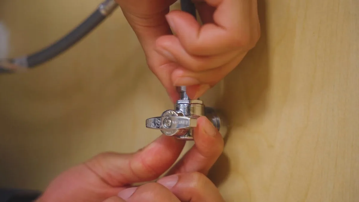 Hands fitting a chrome angle stop valve to a flexible supply line