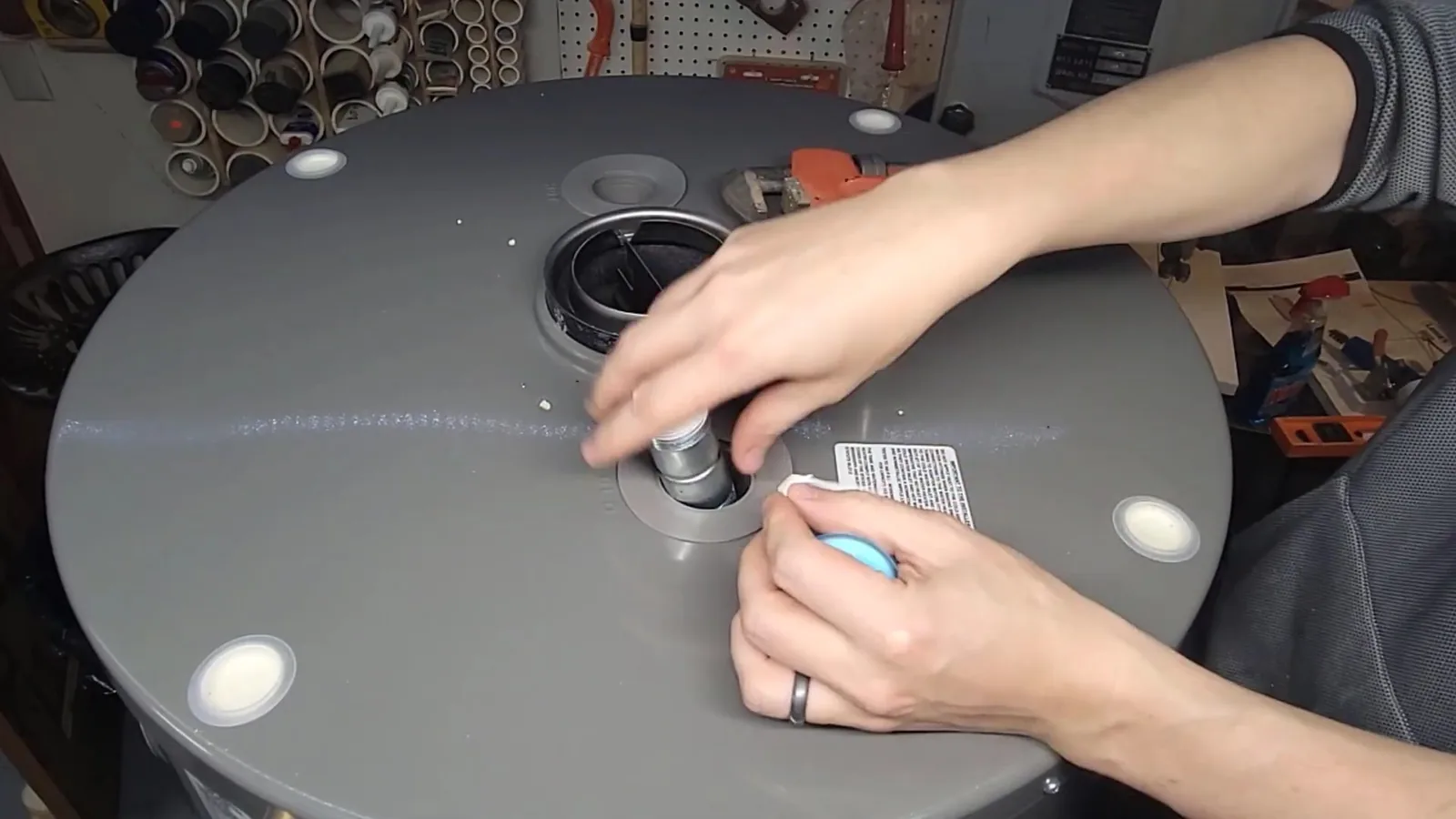 Hands fitting a threaded connector into the fitting on top of a gray tank water heater