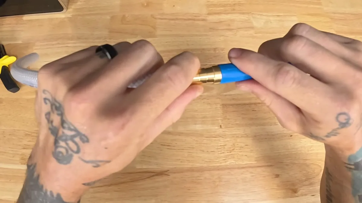 Two hands pushing a blue-handled brass connector onto a flexible hose over a wooden bench