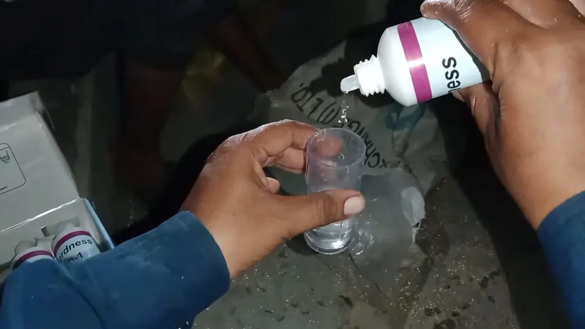 Hand squeezing drops from a small bottle into a glass of water to test its hardness