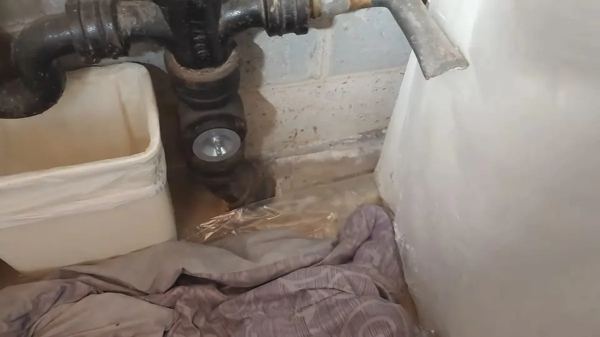 Black cast iron drain trap and fittings against a white wall with a plastic tub below