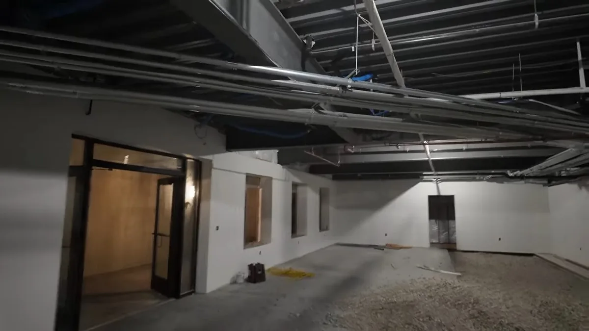 Large unfinished commercial room with overhead pipe runs, bare walls and a gravel floor