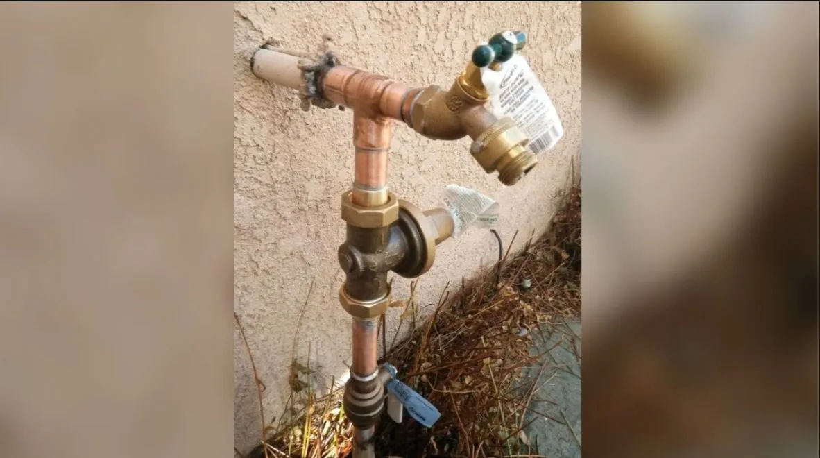 Copper hose bib on a stucco wall with a vacuum breaker on the outlet and a paper tag hanging from it