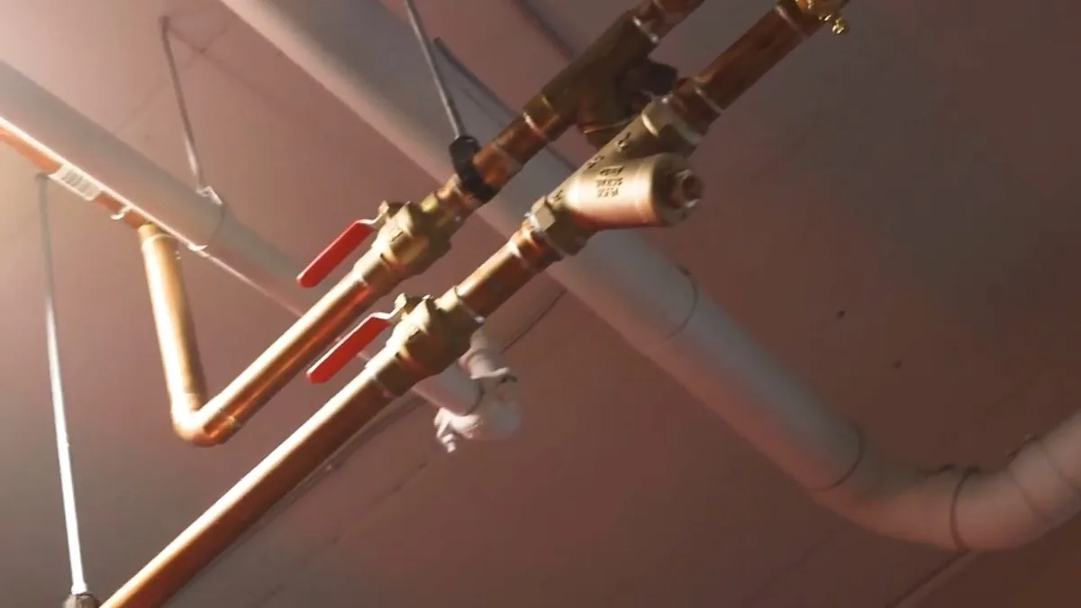 Overhead copper supply risers with red-handled ball valves running along a ceiling beside a white drain pipe
