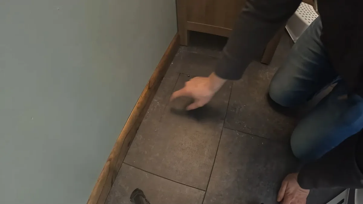 Person kneeling on a dark tile floor with one hand pressed flat on the surface