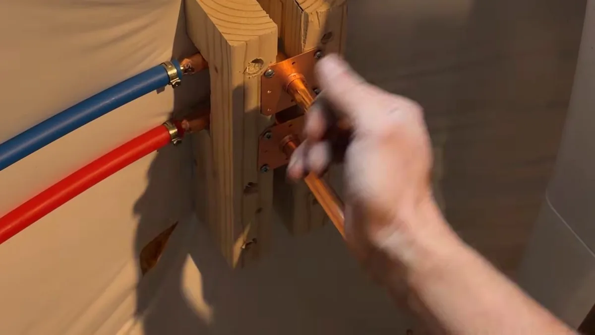 Red and blue PEX lines clamped to wood blocking with a hand reaching toward a copper fitting