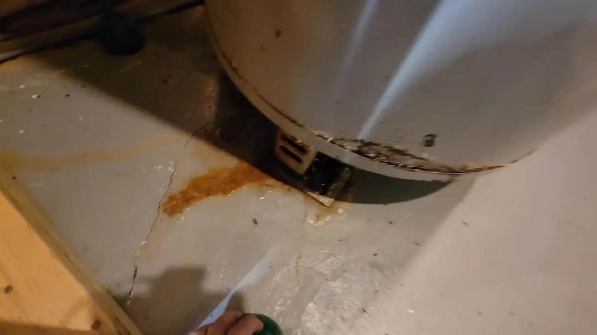 Rust staining and a wet patch on the floor beneath the base of a tank water heater