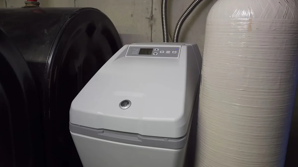 Gray softener cabinet with a digital control head beside a tall white mineral tank