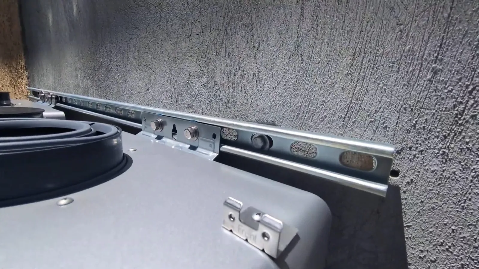 Metal mounting rail fixed to a textured stucco wall above the top of a tankless water heater