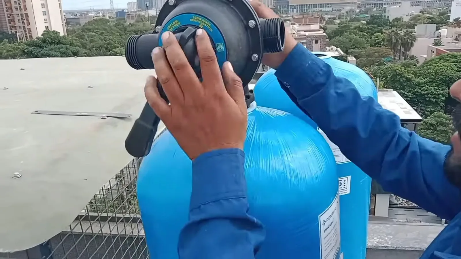 Technician fitting the control valve onto the top of a blue softener tank