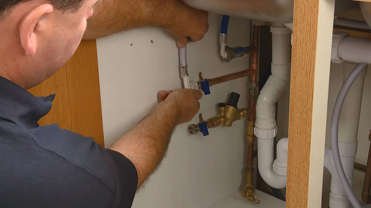 Technician reaching into a sink cabinet to fit a valve and connector on the supply pipes beneath the basin