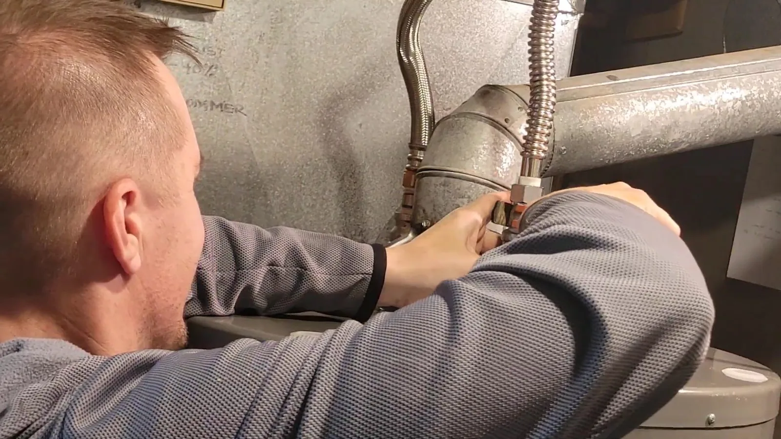 Technician leaning in to work on the flexible connectors at the top of a tank water heater