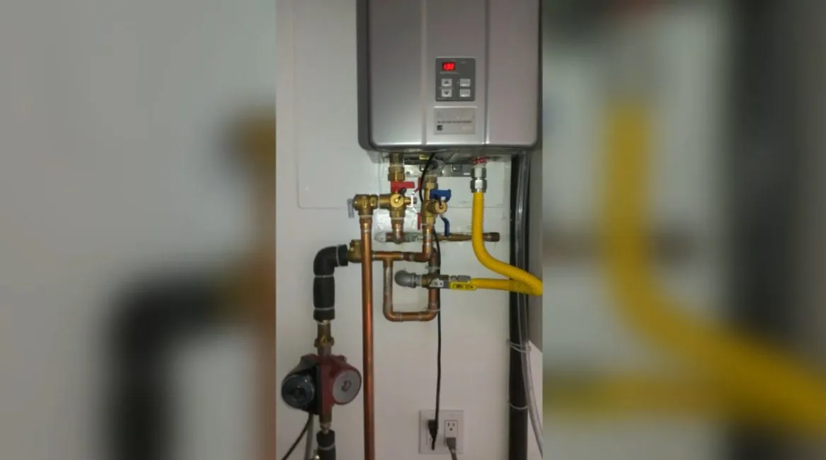 Wall-mounted tankless water heater with copper water lines, service valves and a yellow gas line beneath it