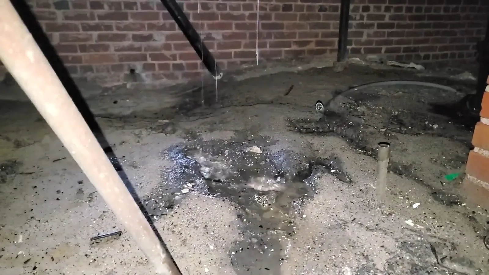 Wet, muddy ground in a brick-walled crawlspace beneath a dripping pipe