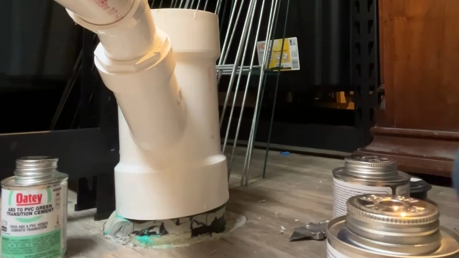 White PVC wye fitting standing on a floor beside cans of cement and primer