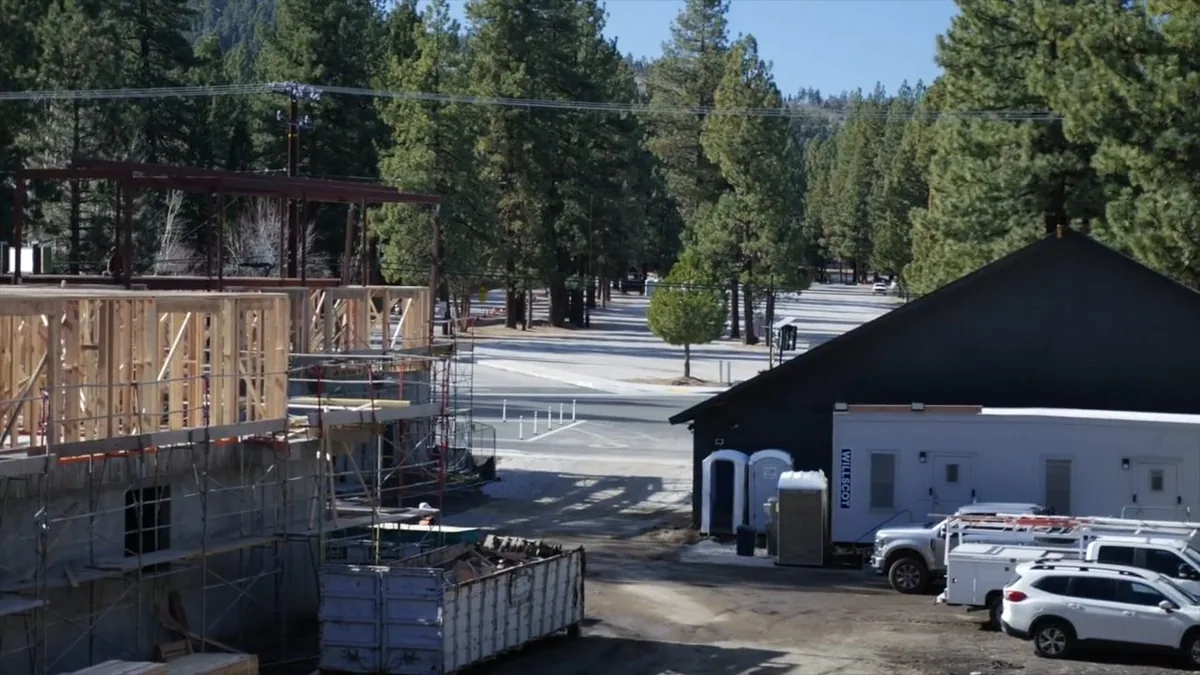 White service vans and a parked car beside a wood-framed building under construction